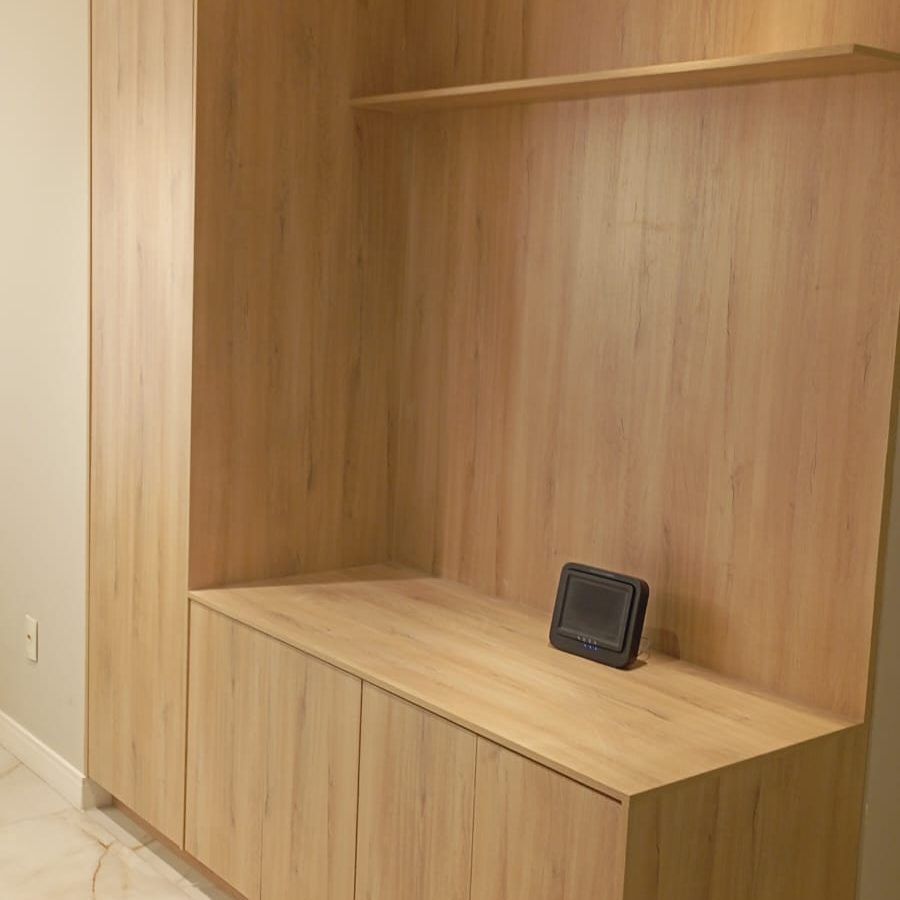 Estante de sala de estar moderna e planejada com várias portas e nichos, feita em MDF com acabamento que imita madeira clara. Projeto Kairós Prime.