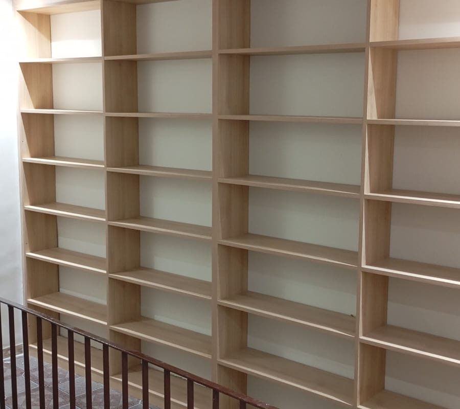 Estante de parede planejada do chão ao teto com vários nichos, ideal para livros e organização vertical. Acabamento em madeira clara. Projeto Kairós Prime.