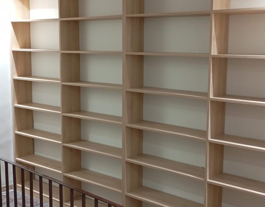 Estante de parede planejada do chão ao teto com vários nichos, ideal para livros e organização vertical. Acabamento em madeira clara. Projeto Kairós Prime.